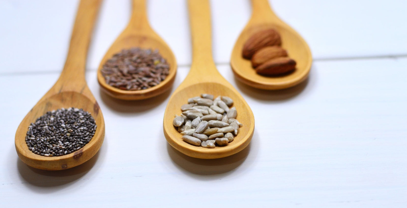 Gesunde Ernährung funktioniert mit Sonnenblumenkernen, Mandeln, Chia Samen und Leinsamen, die auf vier Holzlöffeln aufgehäuft sind.