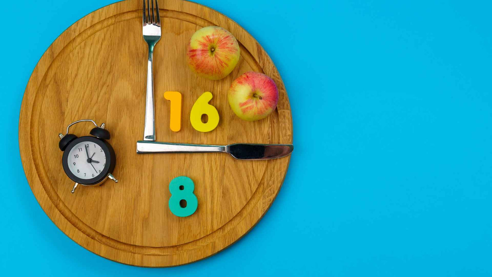 Rundes Brett mit Gabel & Messer als Zeiger, Obst im Viertel zwischen 12 und 3 Uhr, und einem Wecker