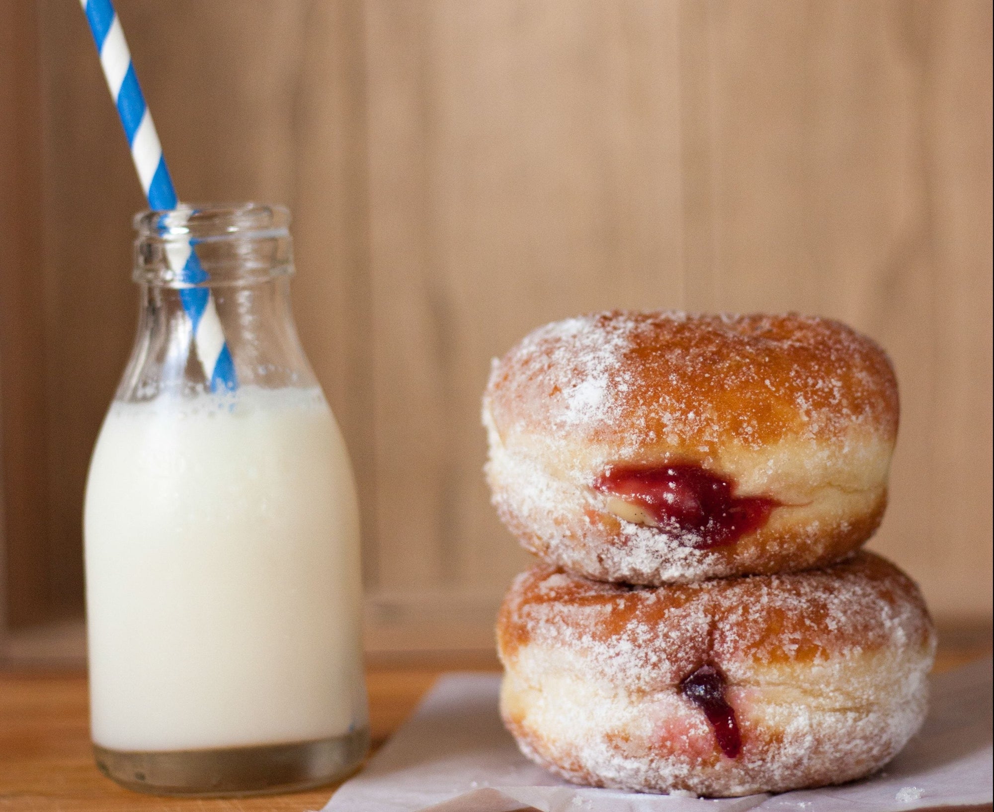 Auf Zucker verzichten ist nicht so einfach: Zwei Krapfen mit Marmeladenfüllung liegen übereinander und daneben steht ein Glas Milch mit einem Strohhalm darin.