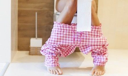 Frau sitzt mit heruntergelassener Hose und Toilettenpapier in der Hand auf Toilette weil sie unter Verstopfung leidet