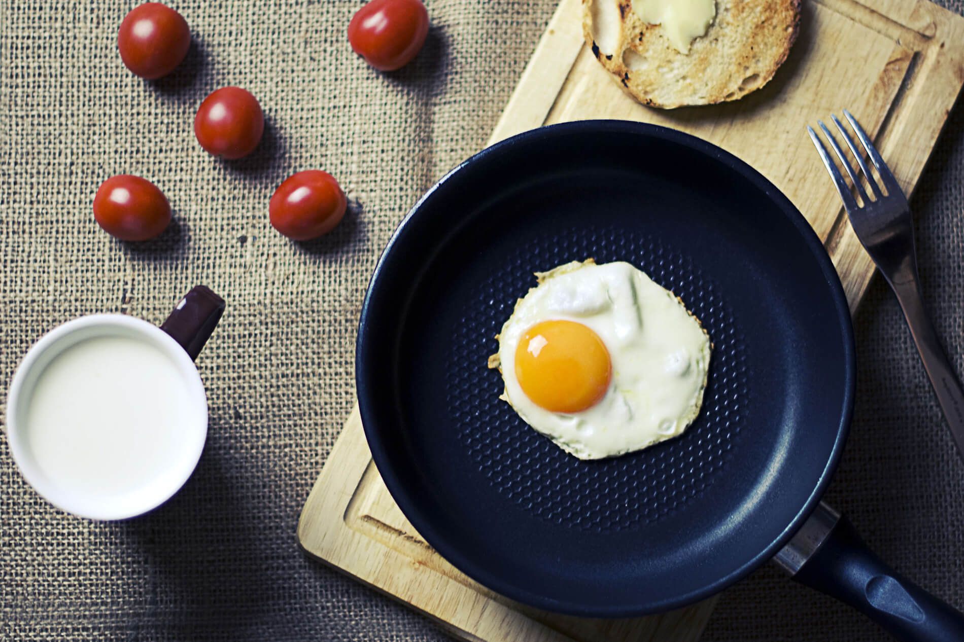 Spiegelei in der Pfanne auf Holzbrett mit Tasse und Tomaten im Hintergrund