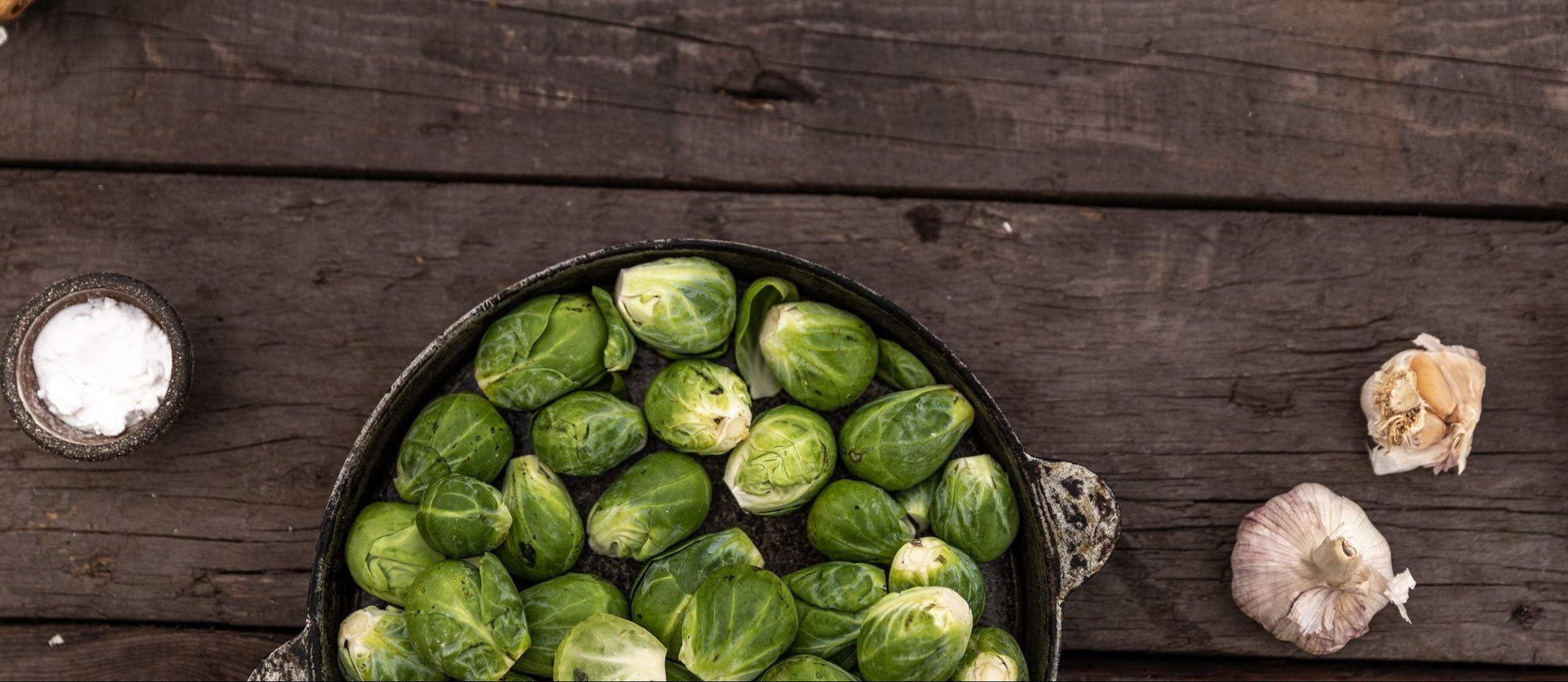 Essen und Gefühle: Rosenkohl in einer Schüssel auf einem Holztisch mit Knoblauch und Salz daneben platziert