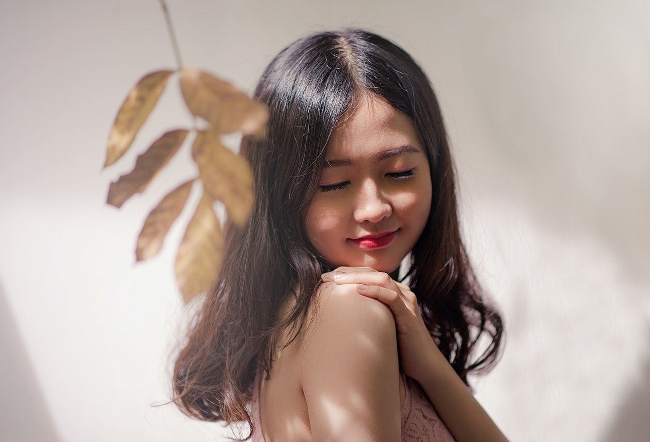 Eine Frau schaut genießend zur Seite und streichelt sich über die Schulter, weil ihre Haut durch TCM Ernährung besser geworden ist. und sie in ihre Gesundheit investiert hat