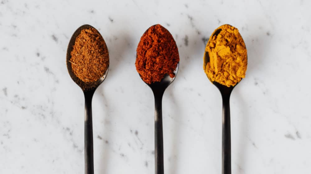 Ernährung und Gehirn gehören zusammen und mit Gewürzen, wie Chili, Kurkuma und Curry, die hier auf drei schwarzen Löffel aufgehäuft sind, kann man seine Gesundheit beeinflussen.