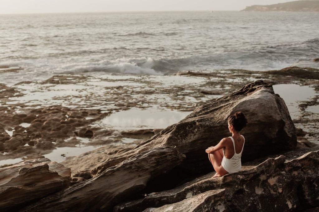 Frau, die nicht vom Jojo-Effekt betroffen ist, sitzt im weißen Top auf Steinen von dem Meer.