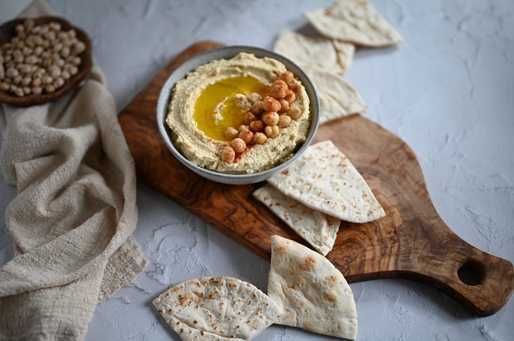 Selbstgemachter Hummus mit Kichererbsen und Öl in einer kleinen Schüssel auf einem Holzbrett, mit arabischem Brot angerichtet