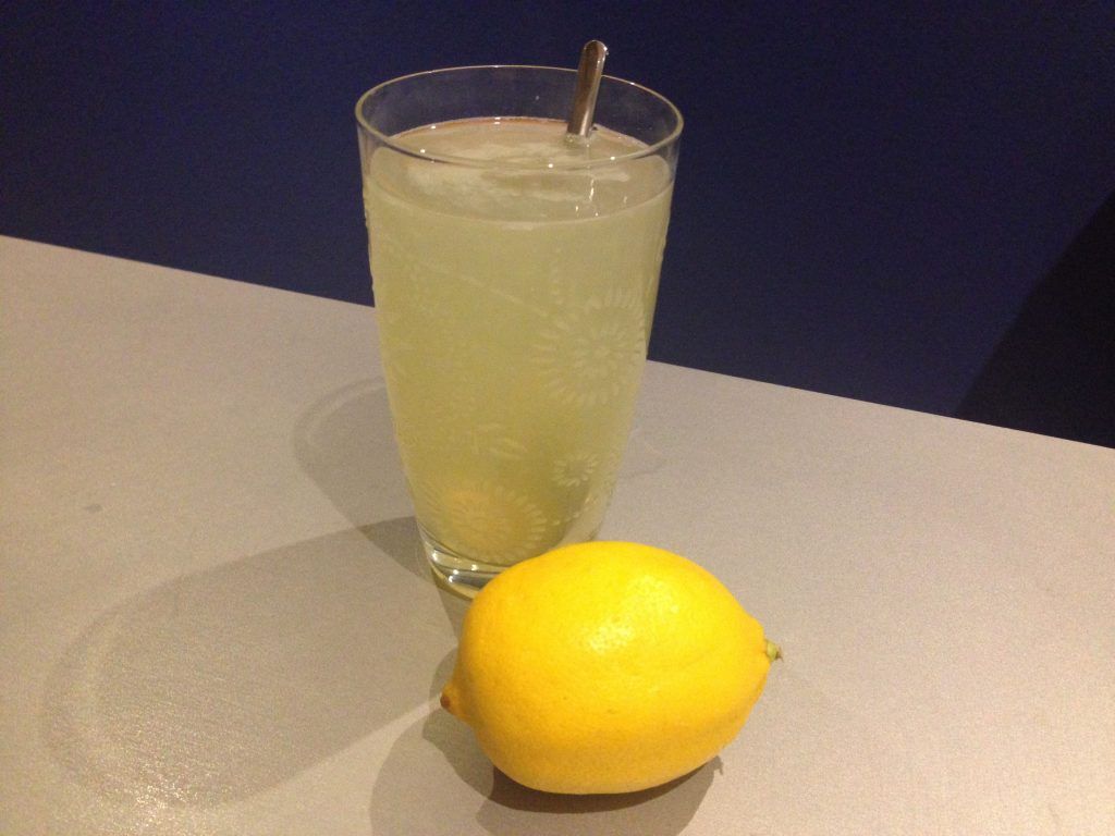 Eine gesunde Zitrone liegt vor einem Glas mit Zitronenwasser.