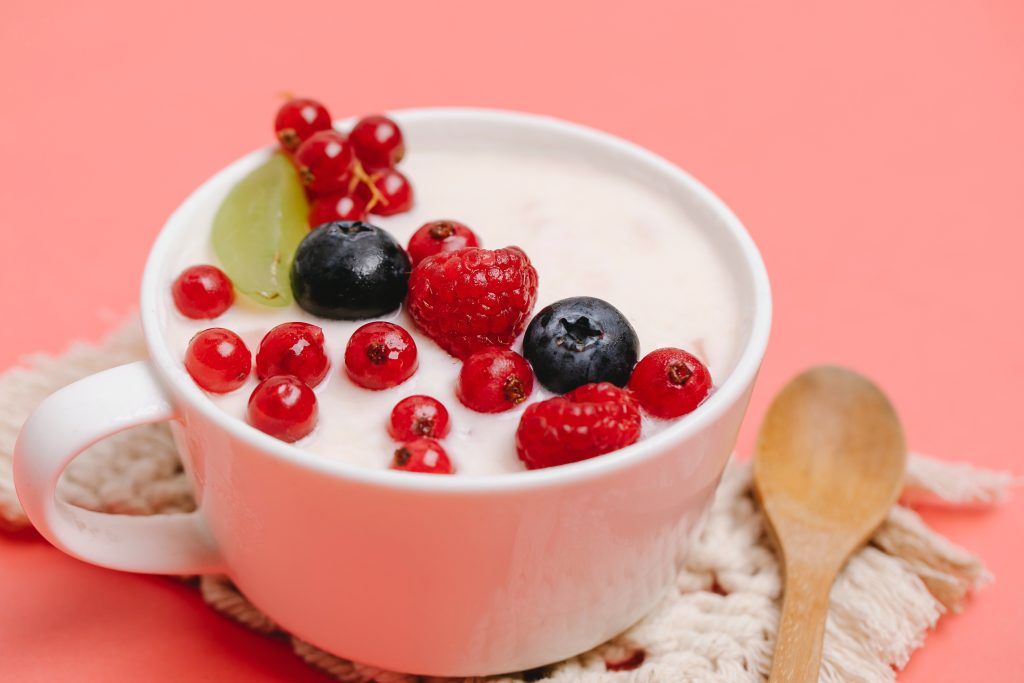 Joghurt angerichtet in Tasse mit Beeren und Holzlöffel daneben macht das Frühstück weglassen unmöglich