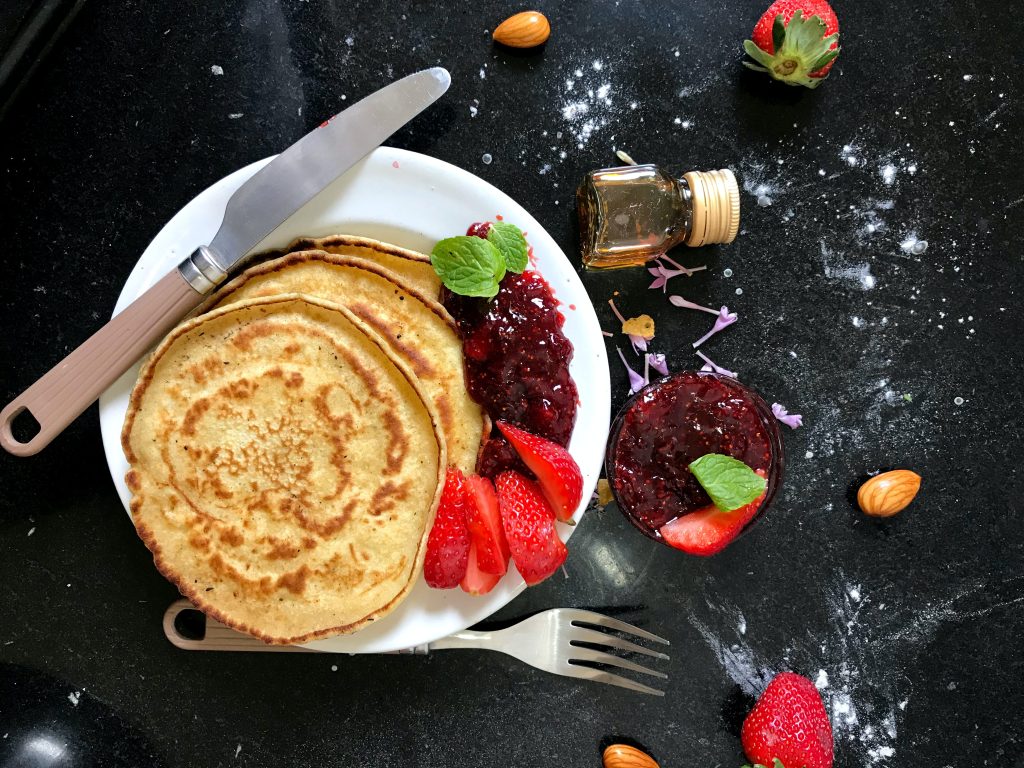 Glutenfreie Pancakes auf Teller mit Erdbeeren und Marmelade verfeinert