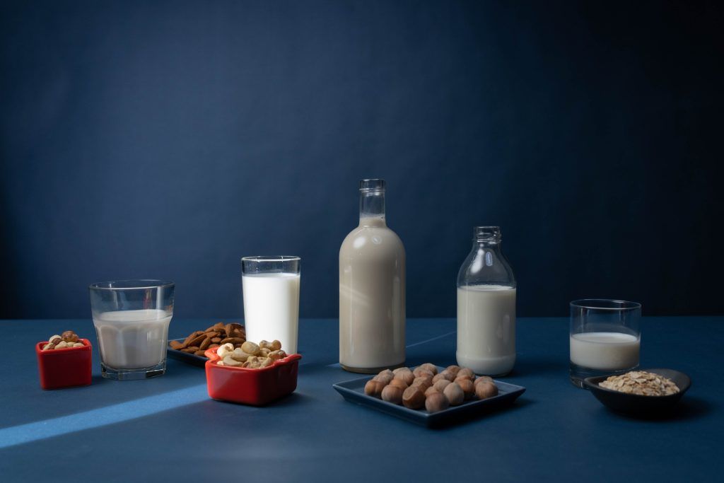Gläser und Flaschen Milch mit Mandeln, weiteren Nüssen und Hafer davor platziert