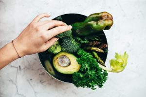 Essen und Gefühle: Rohkost mit Avocado, Paprika, Salat und Brokkoli in einer Schüssel mit einer Hand die danach greift