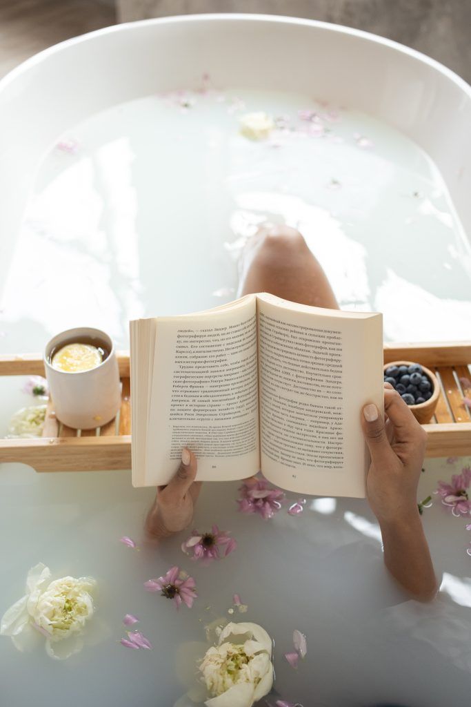 Eine Frau, die einen Ernährungscoach hat, liegt mit einem Buch und einem Cappuccino in der Badewanne.