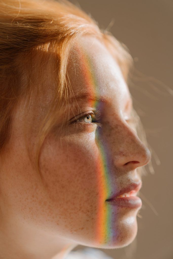 Eine rothaarige Frau mit Sommersprossen, auf deren Gesicht ein Regenbogen reflektiert, hat ihre Haut durch die TCM Ernährung verbessert auf die Psychologie beim Abnehmen geachtet.