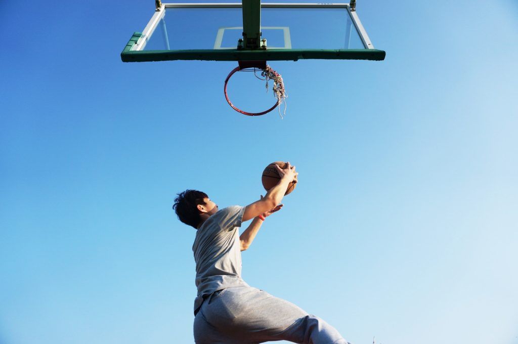 Ein Mann springt hoch zum Basketballkorb, weil er viel Energie von seinem iostonischen Getränk gezogen hat.