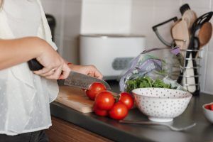 Inneren Schweinehund überwinden und abnehmen: Frau schneidet Tomaten auf einem Brett in der Küche