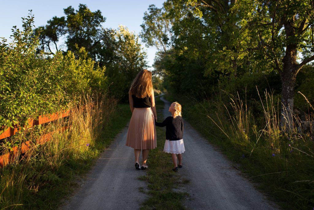 Eine Frau und ein Kind laufen einen Weg zwischen Bäumen und Hecken entlang und investieren in ihre Gesundheit.