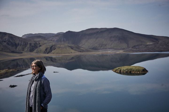 Eine Frau steht vor einem See mit Bergen im Hintergrund.