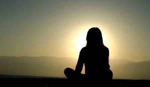 Frau praktiziert Yoga vor untergehender Sonne
