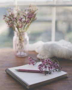Zucker-Diät: Ein Notizbuch liegt mit einem Stift und einer Blume darauf auf einem Tisch mit einer Vase und Blumen im Hintergrund.