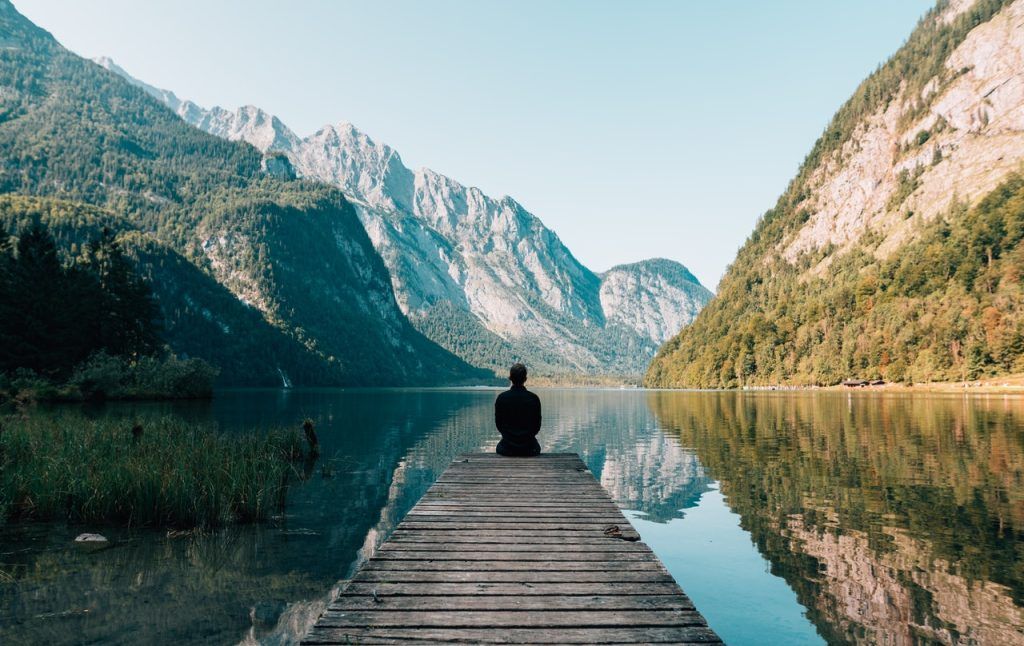 Ein Mensch sitzt auf einem Steg vor einem See, in dem sich die Berge spiegeln und entgiftet seinen Körper von Schwermetallen.