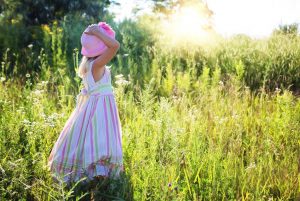 Mädchen mit Kleid und Hut im hohen Gras bei strahlender Sonne