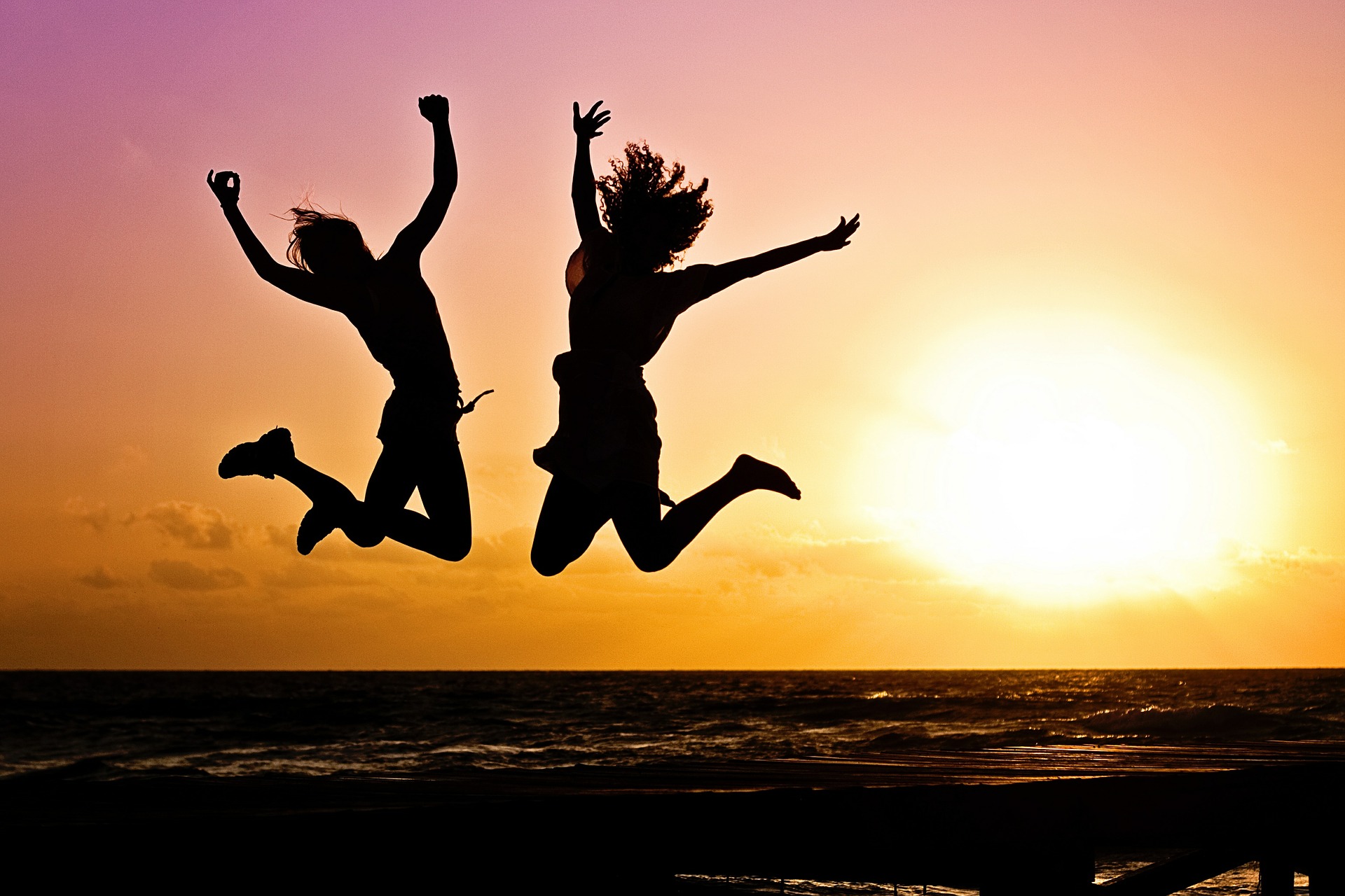 Zwei fröhliche Frauen springen am Strand vor Freude in die Höhe