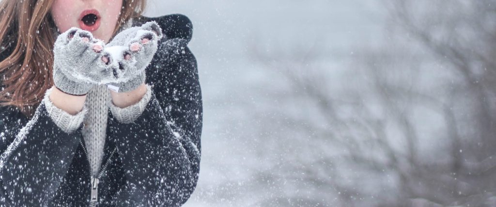 Frau pustet Schnee von ihren Händen und ist draussen