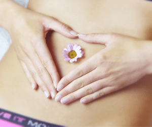 Frau formt Herz mit Gänseblümchen auf dem nackten Bauch