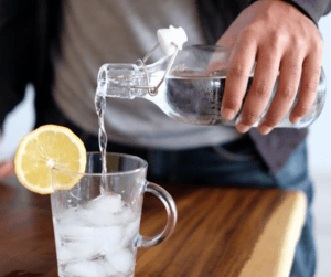 Wasser wird aus einer Glasflasche in ein Glas mit Eiswürfeln eingeschenkt