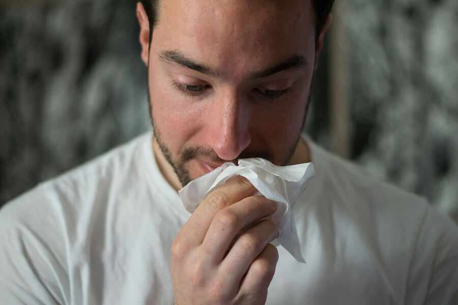 Mann putzt seine Nase weil er unter Heuschnupfen leidet
