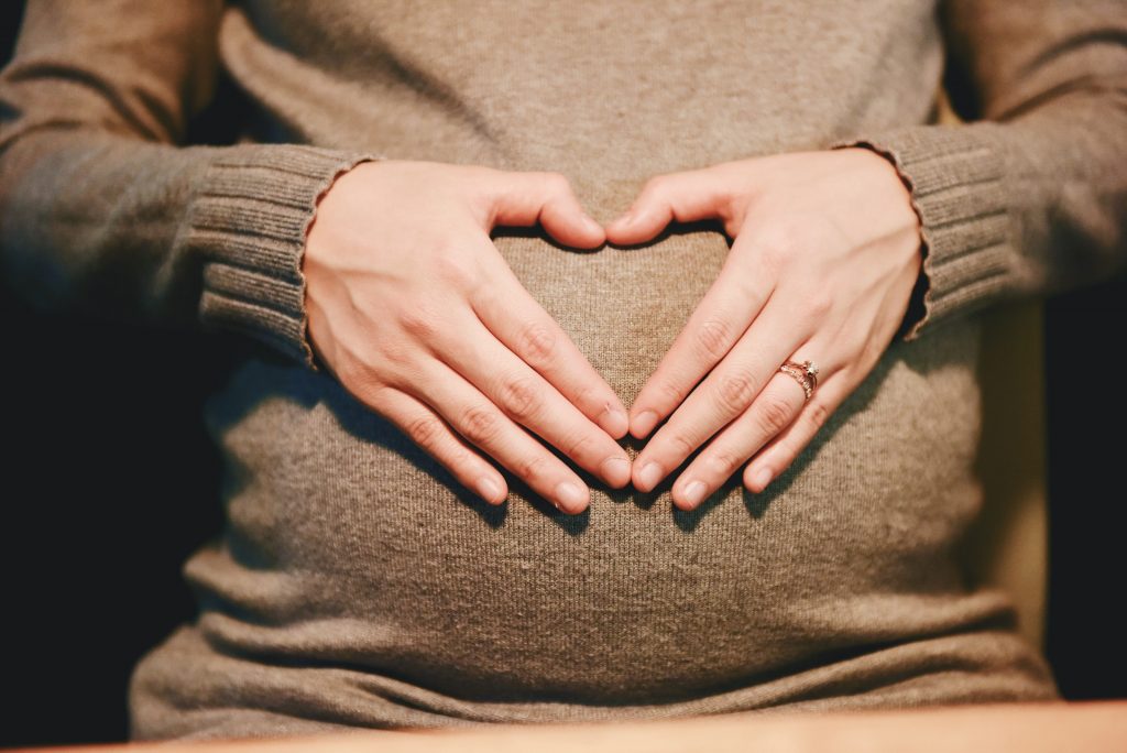 Werdende Mutter formt mit ihren Händen ein Herz auf ihrem Babybauch