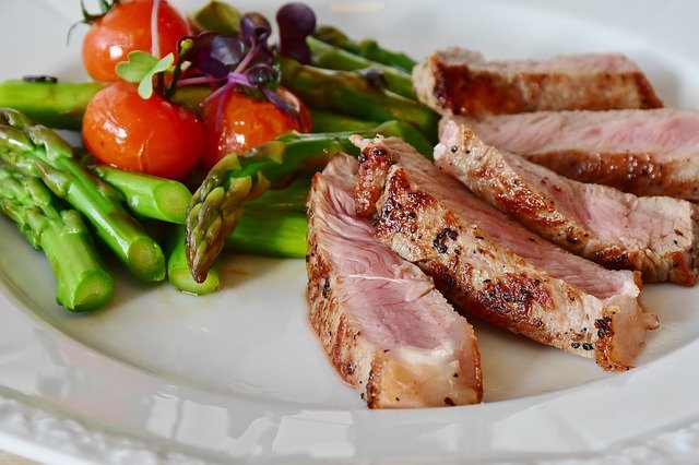 Echte Nahrungsmittel wie Spargel, Fleisch und Tomaten auf einem Teller helfen dem Darm beim abnehmen.