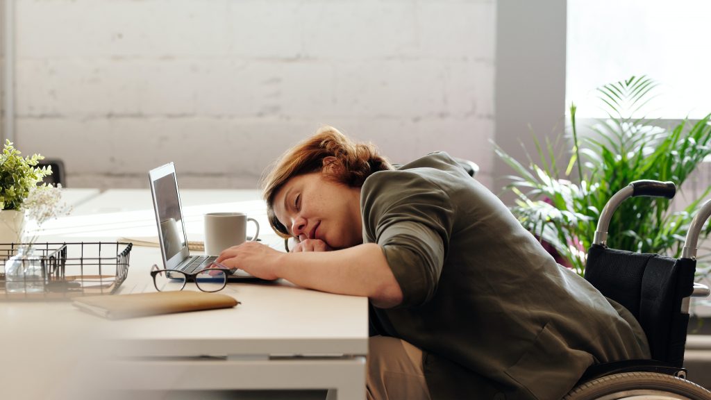 Müde, erschöpfte Frau, die am Arbeitstisch schläft vor Laptop, Brille und Kaffeetasse