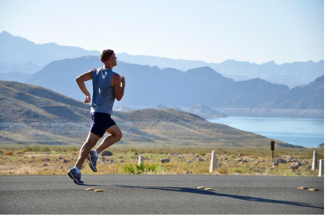 Ein Sportler läuft auf einer Straße durch Berglandschaft und hat genug Kraft durch das L-Glutamin.
