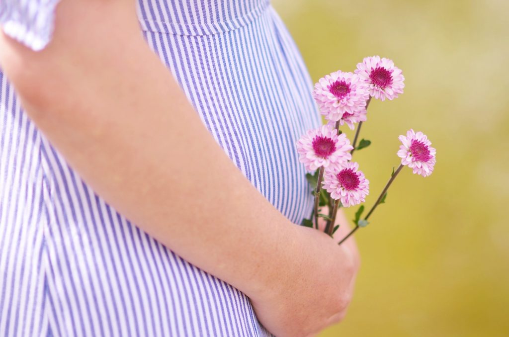 Schwangere Frau hält sich Blumen vor Babybauch