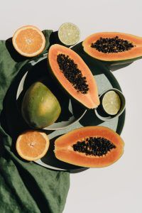 Frische Früchte, wie Papaya, Orangen und Limetten, die hier auf einem dunkelgrünen Tablett über einem grünen Tischtuch aufgeschnitten liegen, gehören zu einer gesunden vegetarischen oder Veganer Ernährung.