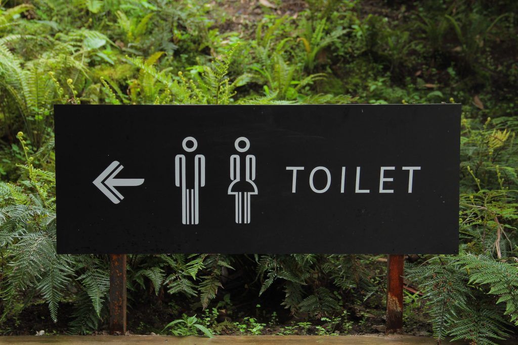 Schild zur Toilette vor tropischem Hintergrund