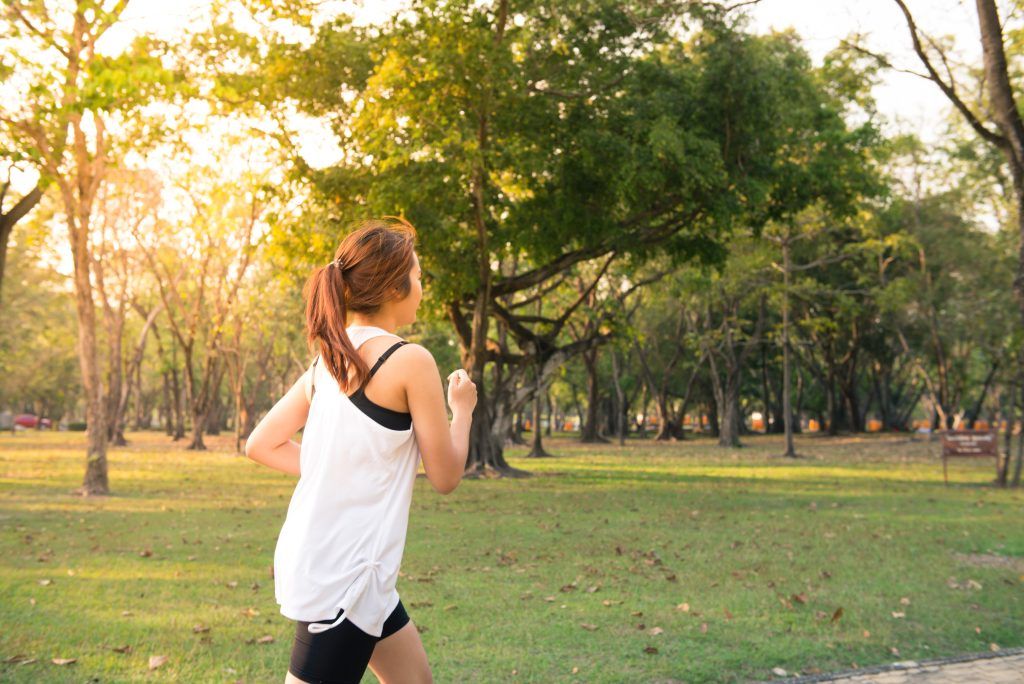 Frau investiert in ihre Gesundheit und joggt durch den Park bei Sonnenschein.