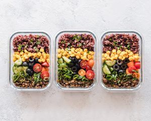 Tipps für gesunde Ernähung: Drei Bowls mit Tomaten, Kichererbsen, Frühlingszwiebeln und Oliven stehen vorbereitet auf dem Tisch für jemanden, der keine Zeit für gesunde Ernährung hat.