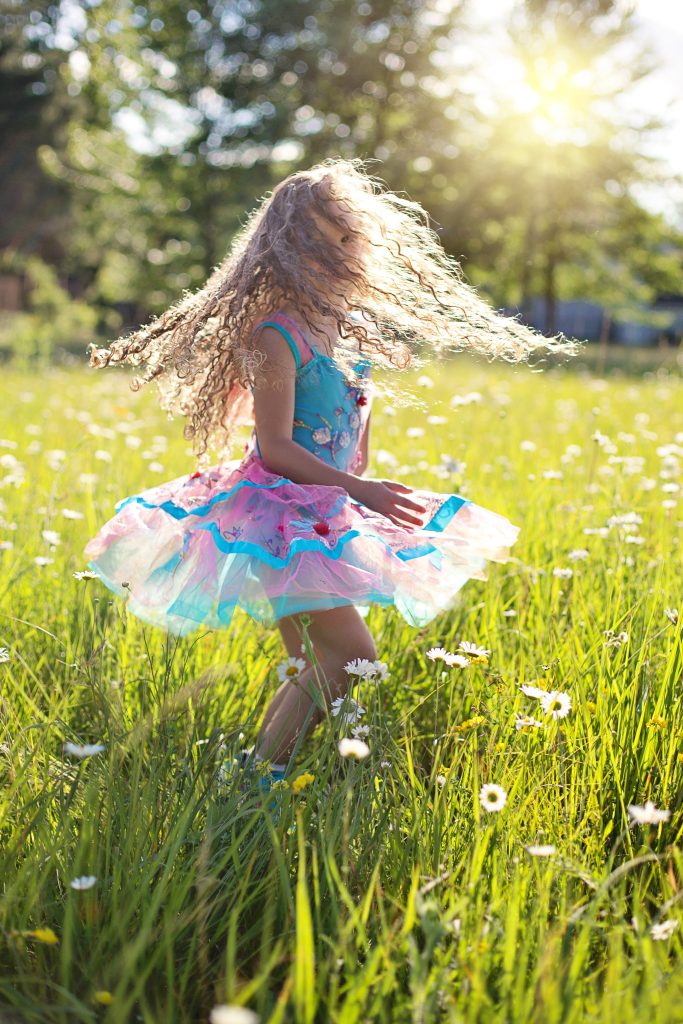 Ein Kind ist gut gelaunt dank Ernährungsumstellung und tanz in einem blau-rosa Kleid in einer Blumenwiese.