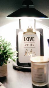 Der motivierende Satz "love your life" pinnt auf einem Klemmbrett unter einer Lampe und davor steht eine Kerze.