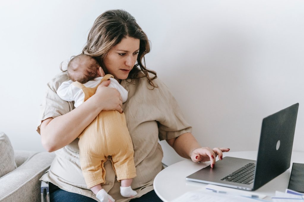 Eine besorgte Mutter mit Baby auf dem Arm recherchiert am Laptop im Internet nach Beikost.