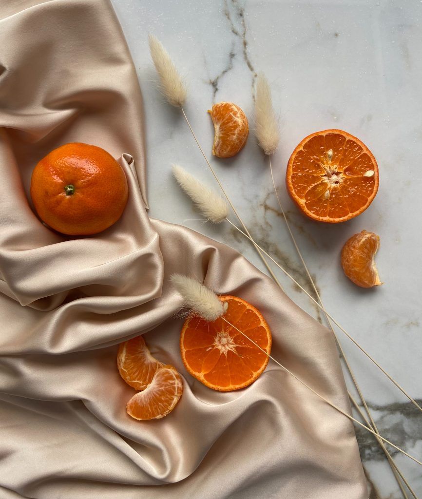 Orangen, die von einem Ernährungscoach empfohlen wurden, liegen mit einem Satin-Tuch und Trockenpflanzen auf einem Marmortisch.