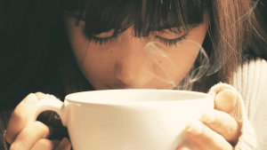 Blähungen lindern mit heissem Tee in Teetasse Frau riecht an Dampf