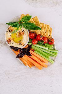 Abnehmen und Ernährung: Hummus mit Olivenöl in einer Schüssel und Gemüsesticks und Knäckebrot angerichtet
