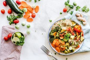 Weniger essen und Abnehmen mit der richtigen Ernährung funktioniert mit einem bunten Salat aus Karotten, Brokkoli, Couscous und Paprika, der in einer Schüssel auf einem Tisch zwischen verteiltem Gemüse liegt.
