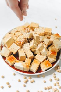 Tofu Stücke in einer Schüssel werden mit Toppings verfeinert